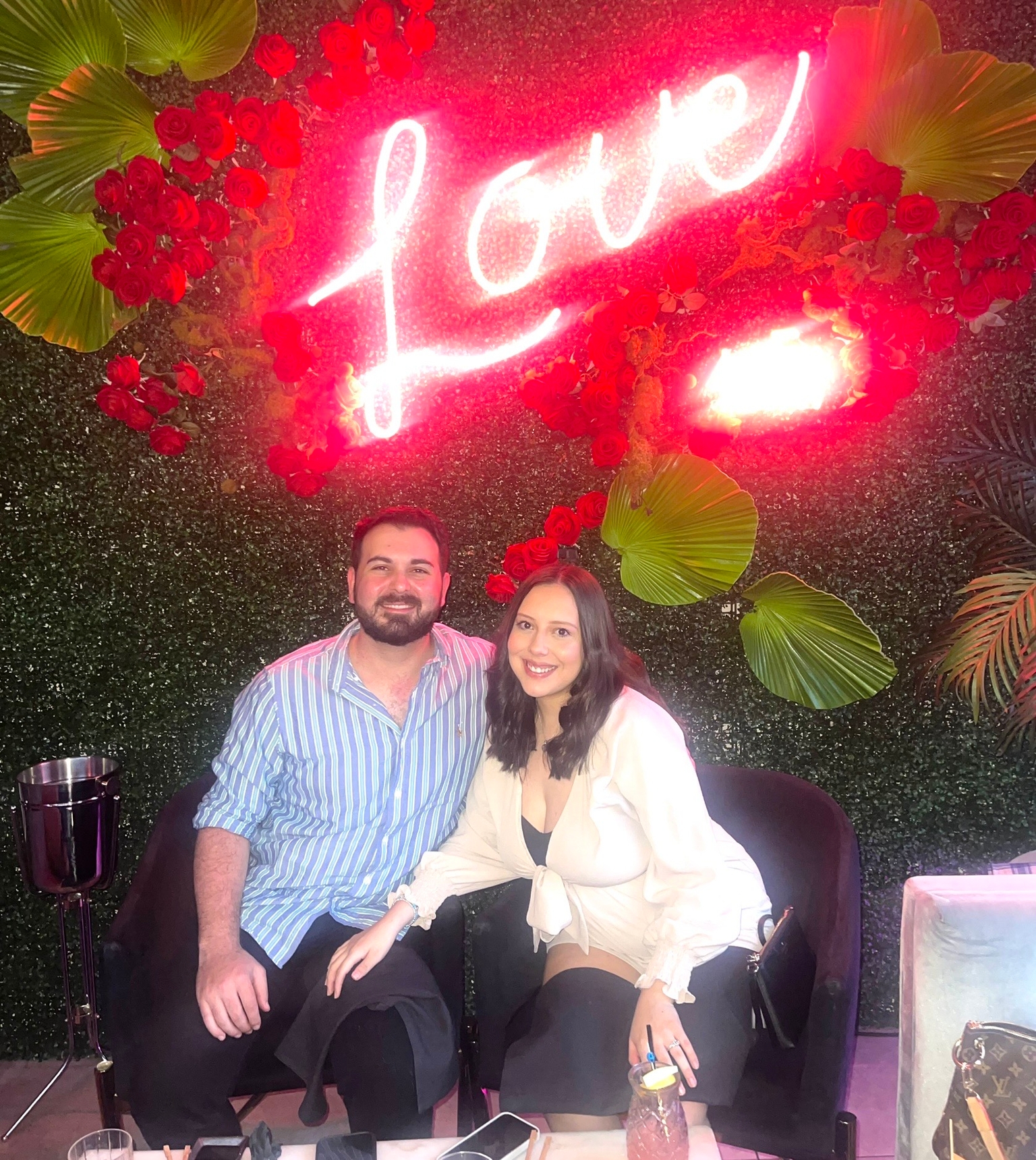 Zayra & Matt in front of a neon sign that says Love